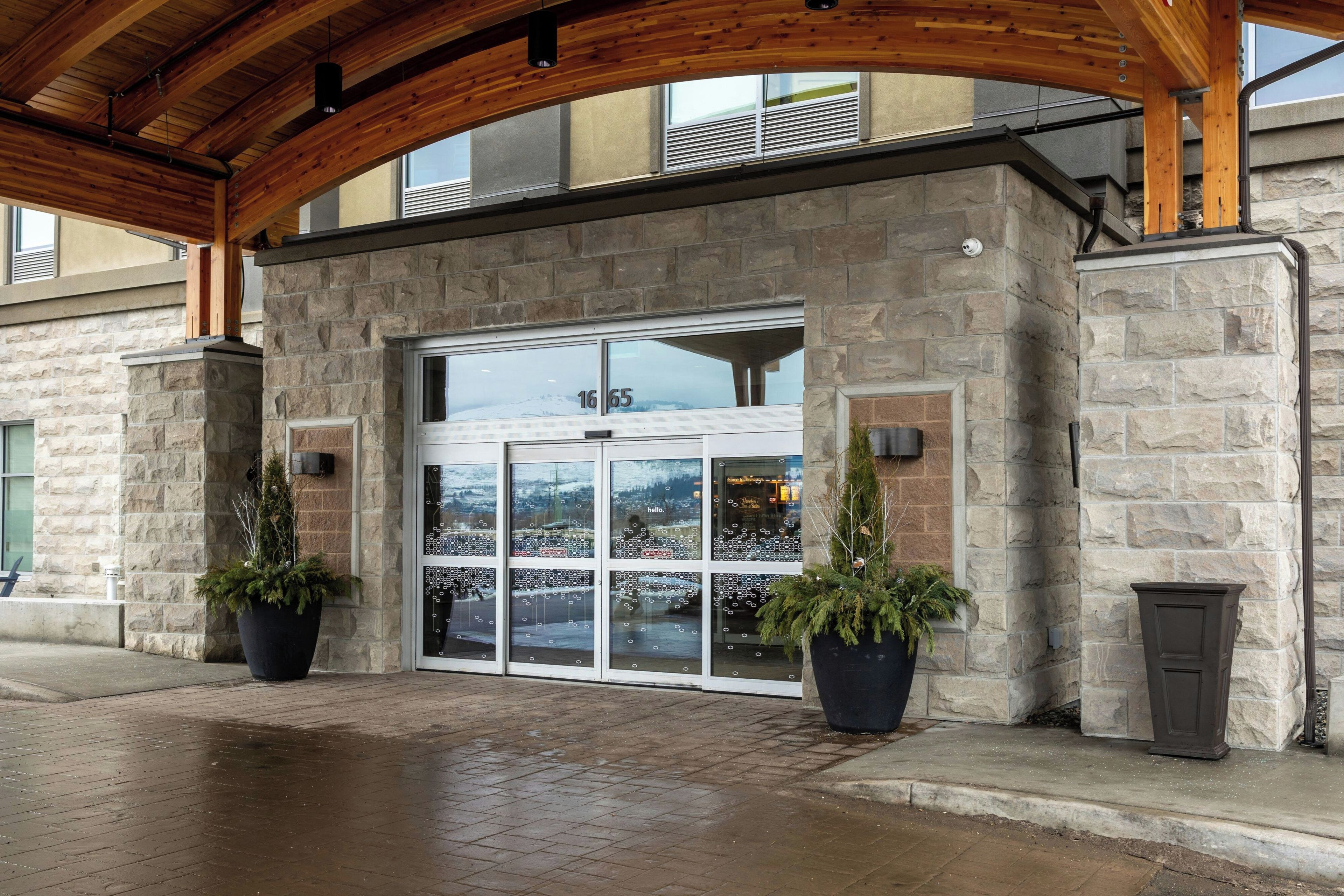A stone building with a large glass door, potted plants, and a wooden ceiling.
