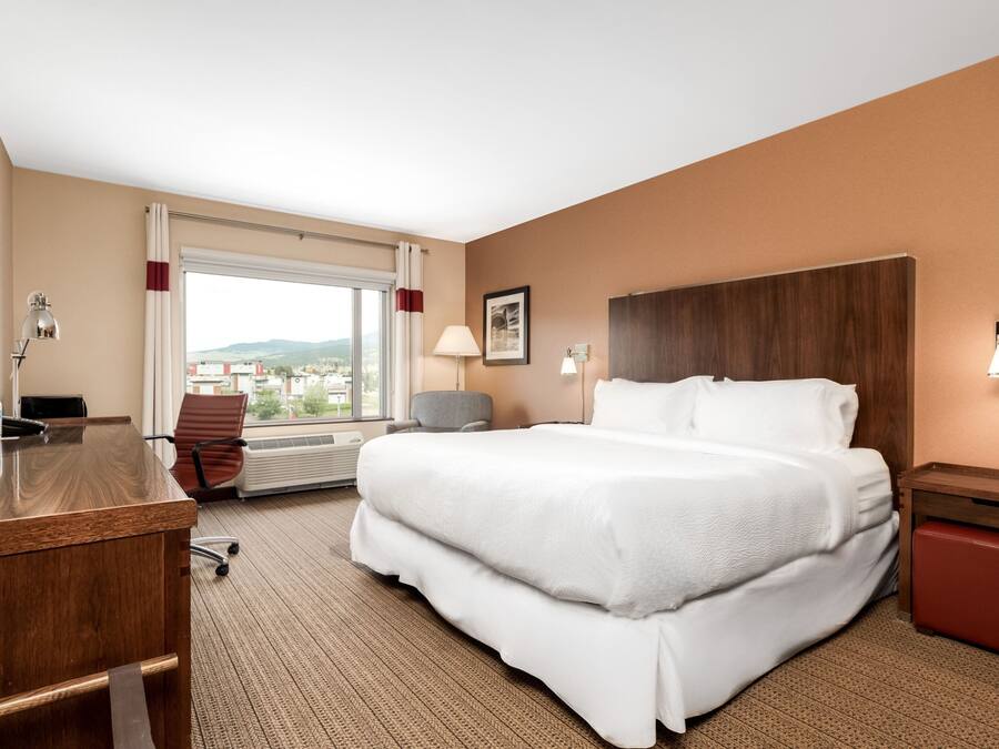 Ein Hotelzimmer mit einem großen Bett, einem Schreibtisch, einem Stuhl, einem Fenster mit Blick und einem hölzernen Kopfteil.
