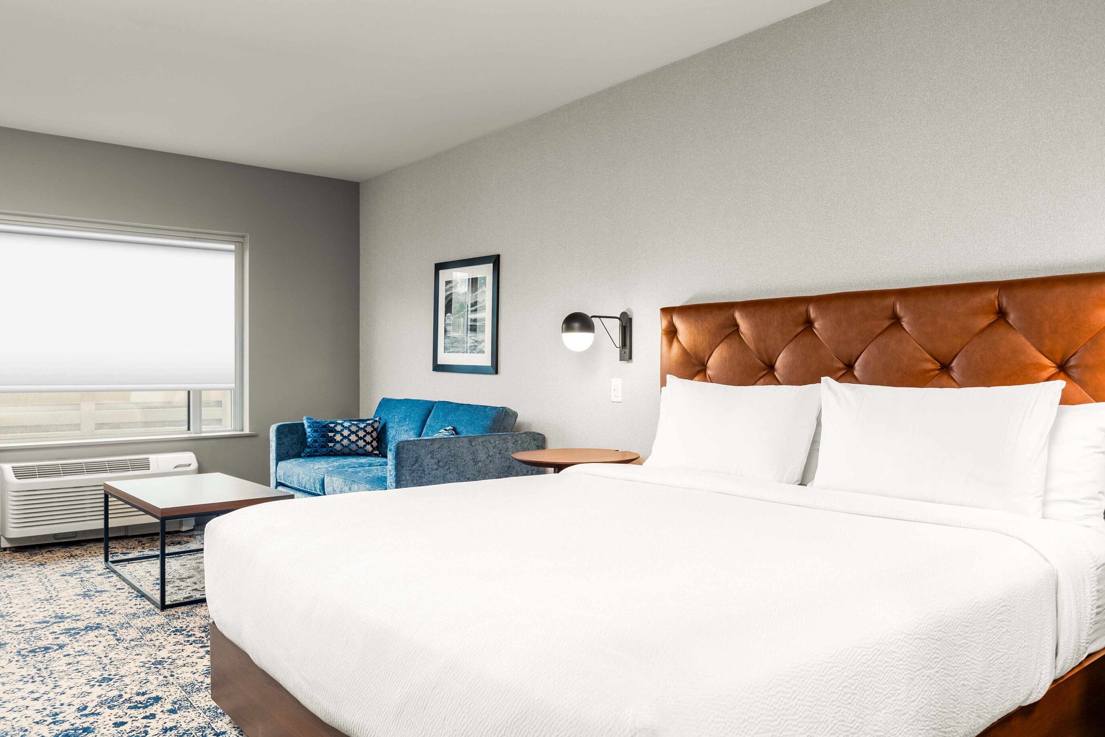 Ein Hotelzimmer mit einem großen Bett, einem blauen Sofa, einem kleinen Tisch und einer Wandlampe.