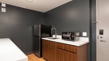 A compact kitchen with a black refrigerator, a microwave, and a sink on a white countertop.