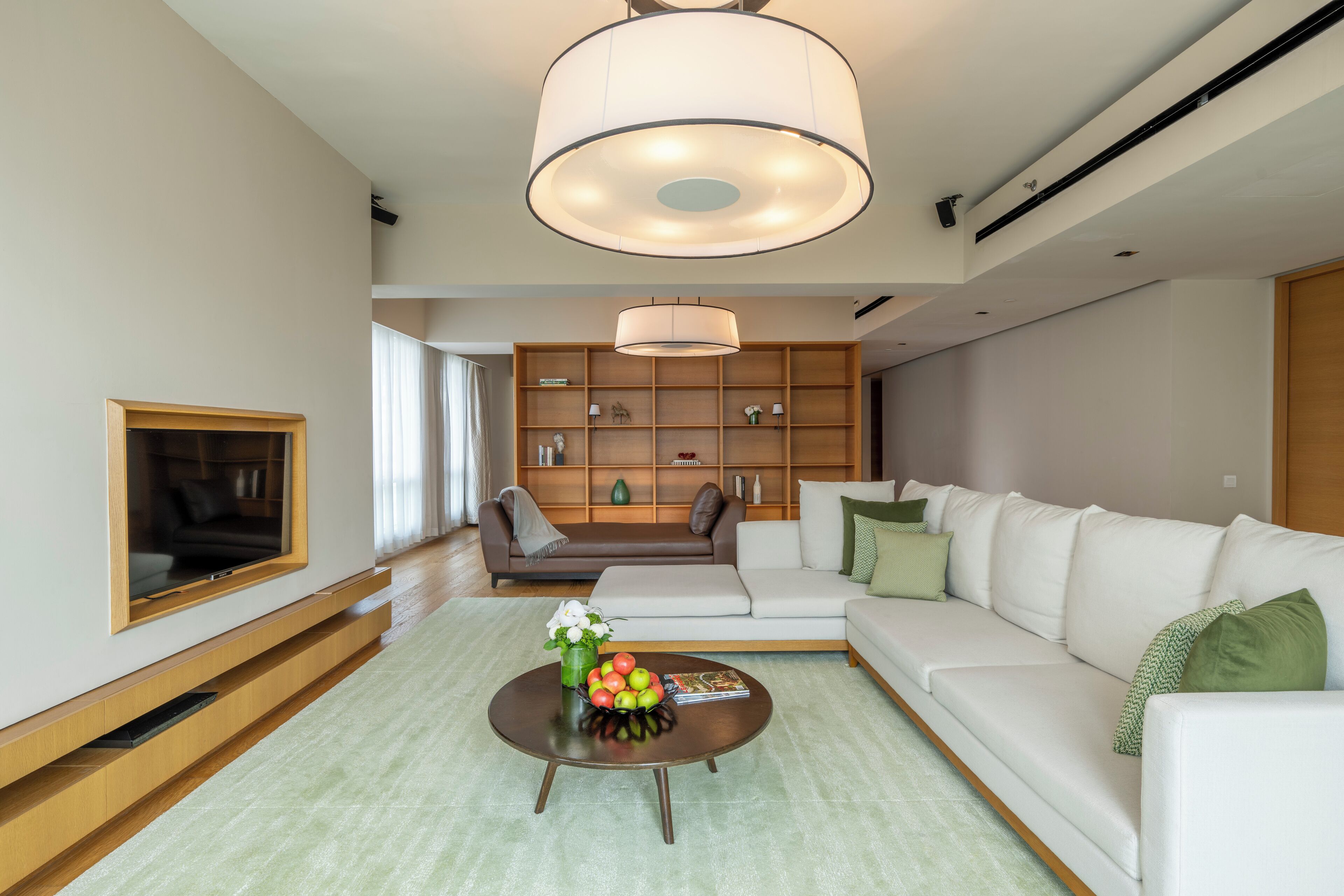 A modern living room with a sofa, a coffee table with decorative items, a bookshelf, and a large ceiling light.