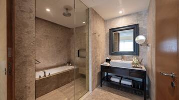 A modern bathroom with a glass-enclosed shower, a freestanding bathtub, a vanity with a mirror, and a wooden door.