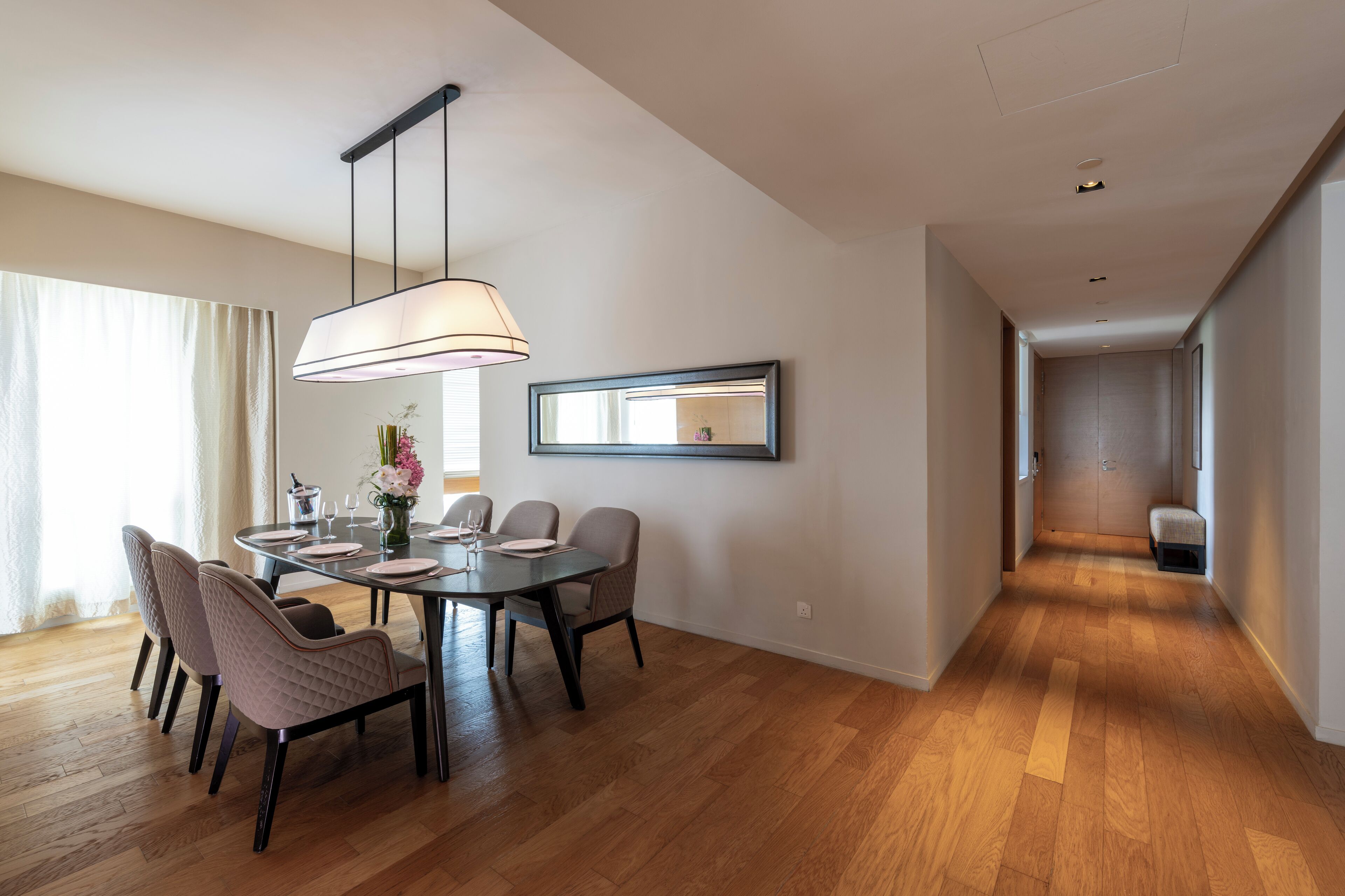 Une salle à manger spacieuse avec un plancher en bois, un lustre moderne et une table à manger dressée pour quatre personnes.