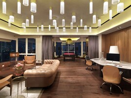 A modern hotel room with a pool table, leather sofa, and a dining area with a marble table.