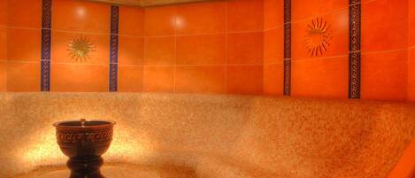 A spa room with a mosaic wall, a decorative bowl, and a sun emblem.