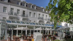 Un hôtel doté d’une véranda en verre, d’une terrasse et d’une façade blanche.