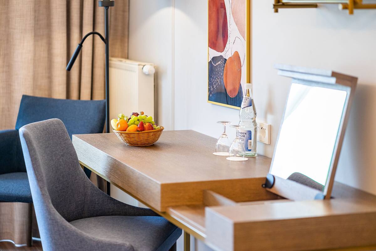 Een moderne hotelkamer met een houten tafel, een schaal fruit, een waterfles en een ingelijste foto.