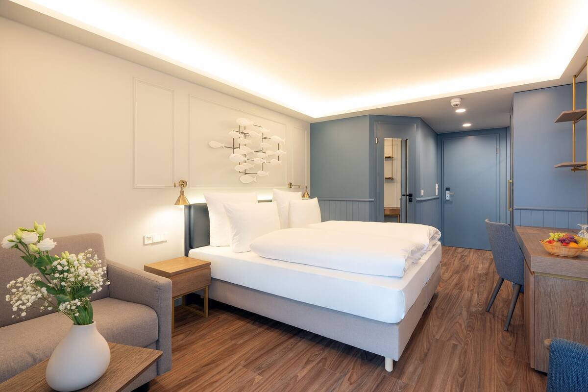 Een moderne hotelkamer met een groot bed, een nachtkastje, een stoel, een bureau met een fruitmand en een vaas met bloemen.