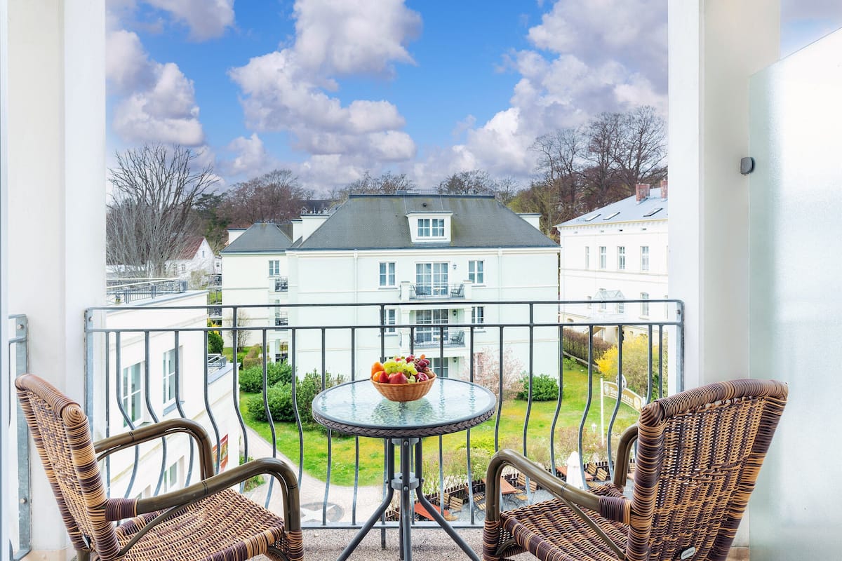 Een balkon met rieten stoelen, een klein rond tafeltje en een schaal fruit.