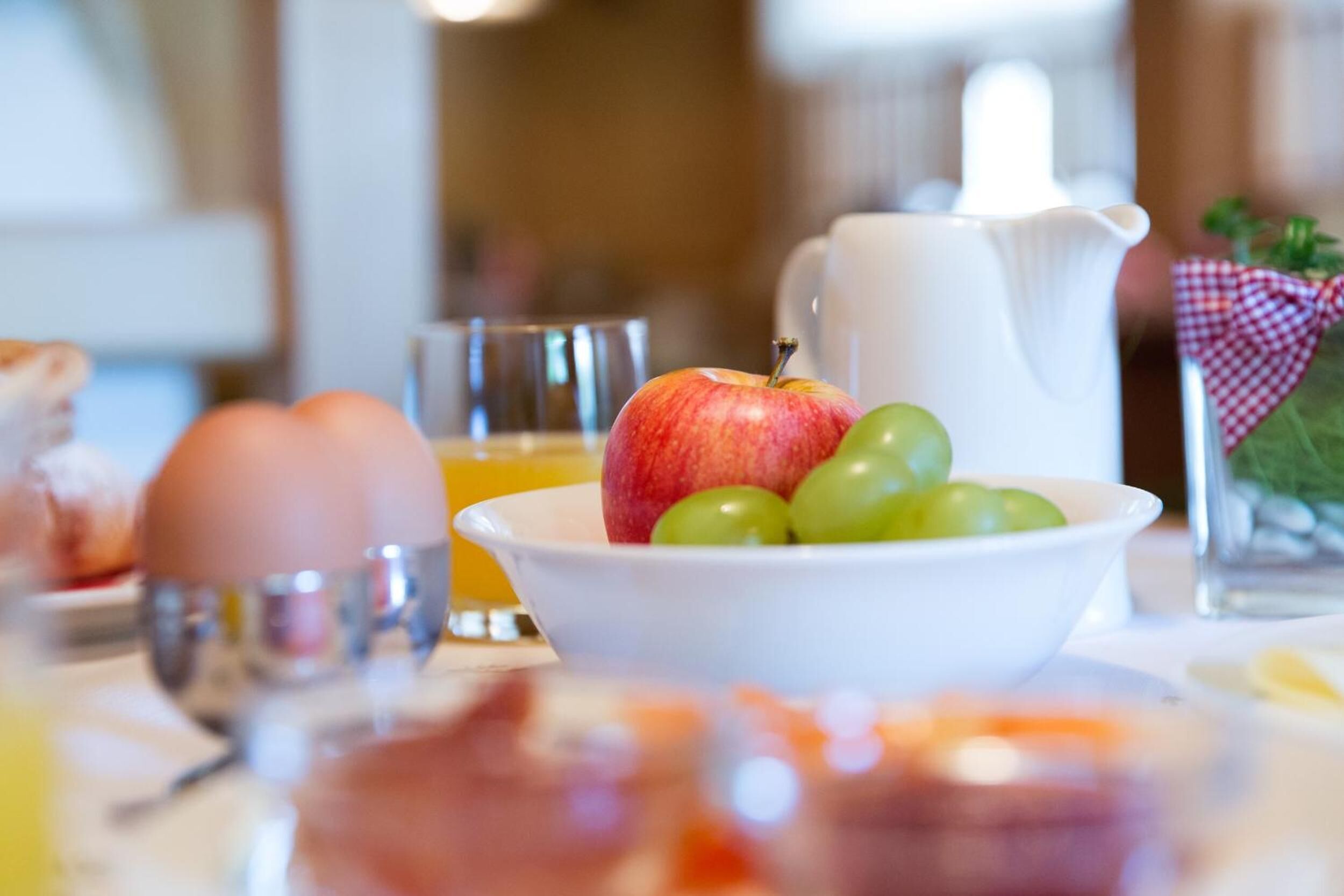 Ein Frühstückstisch mit einer Fruchtschale, einer Karaffe und einem Glas Orangensaft.