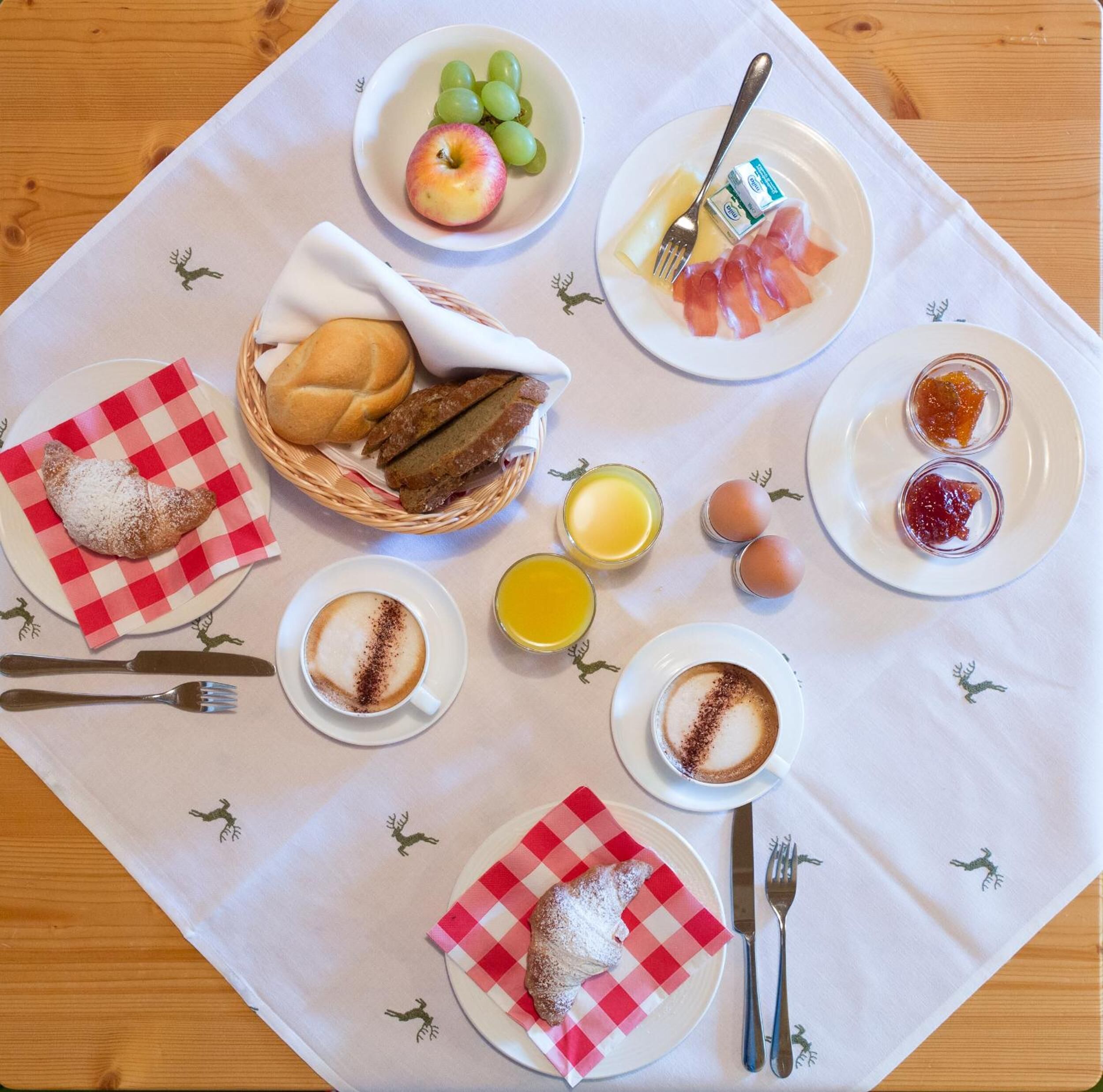 A breakfast setting with croissants, a basket of bread, a plate of ham and cheese, a bowl of grapes, a plate of eggs, and a cup of coffee.