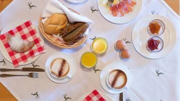 A breakfast setting with croissants, a basket of bread, a plate of ham and cheese, a bowl of grapes, a plate of eggs, and a cup of coffee.