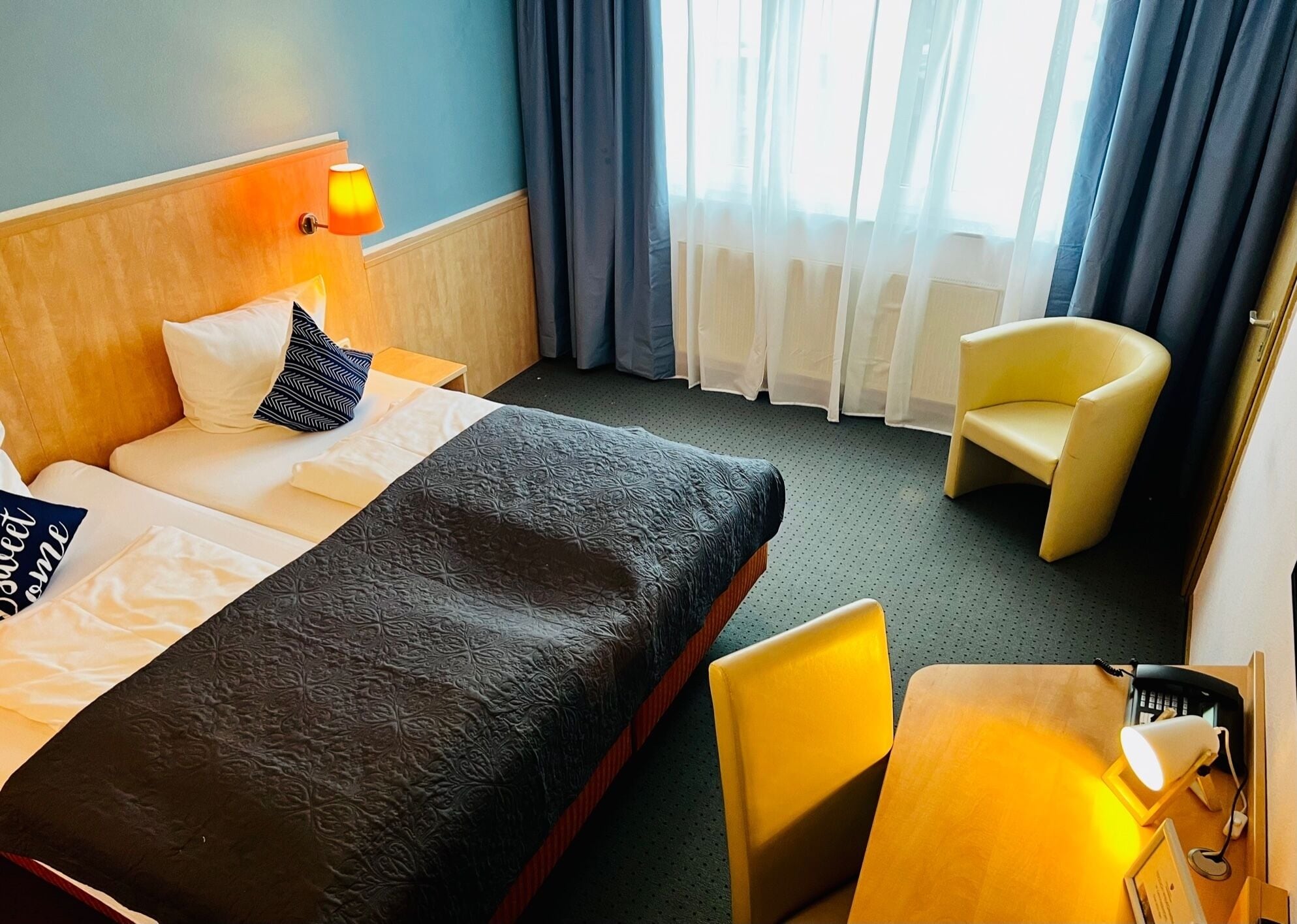 Habitación de hotel con una cama, dos almohadas, una lámpara de noche, una silla, un escritorio y un teléfono.