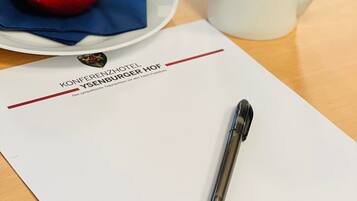 A hotel brochure with a pen, a red apple, and a white mug on a table.