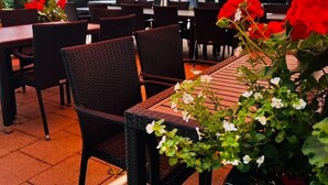 Een terras met tafels en stoelen onder oranje parasols, omgeven door potplanten en een stenen muur.