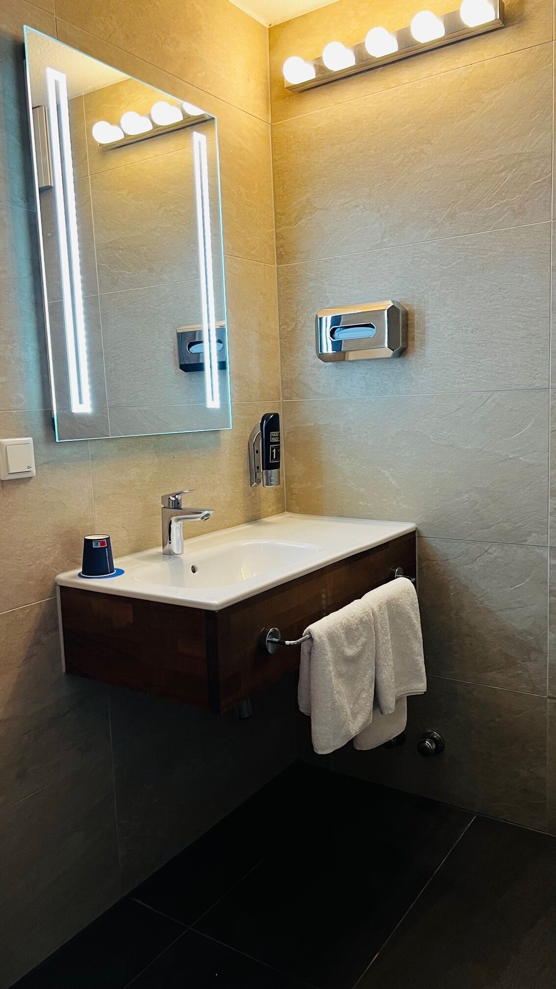 A modern bathroom with a large mirror, vanity, and a towel rack.