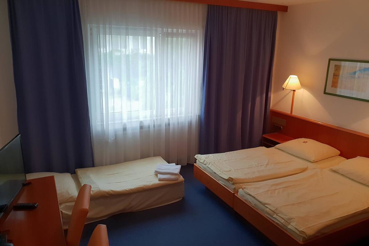 A hotel room with two beds, a desk, a chair, a lamp, and a window with curtains.