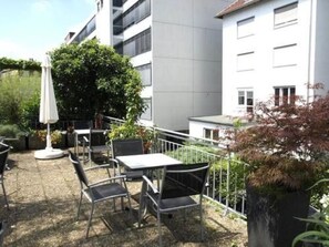 An outdoor patio area with tables and chairs, surrounded by a metal railing, and adjacent to a building with multiple windows. - City Hotel Stuttgart (Stuttgart)