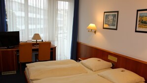 A hotel room with a bed, a desk with a chair, a television, and a lamp. - City Hotel Stuttgart (Stuttgart)
