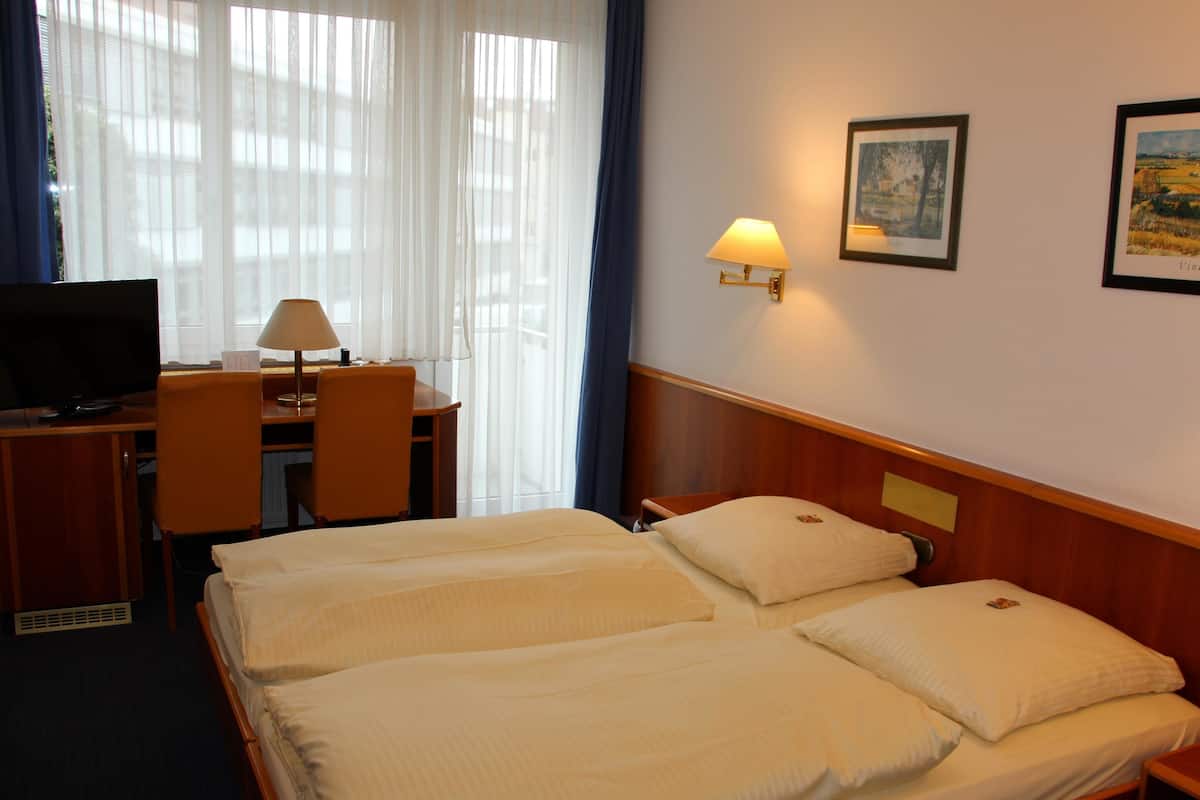 A hotel room with a bed, a desk with a chair, a television, and a lamp.