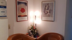 A hotel lobby with two brown leather armchairs, a wall-mounted light, and two framed pictures. - City Hotel Stuttgart (Stuttgart)