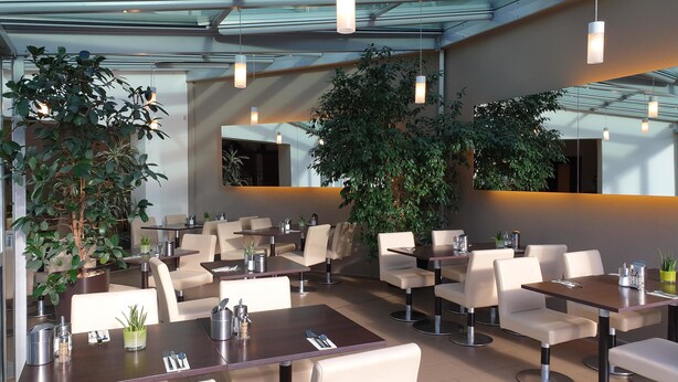 A modern restaurant with glass ceilings, indoor plants, and contemporary furniture. - City Hotel Stuttgart (Stuttgart)