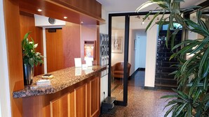 A reception area with a wooden counter, a clock, a plant, and a staircase in the background. - City Hotel Stuttgart (Stuttgart)