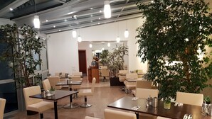 A modern dining area with multiple tables and chairs, potted plants, and pendant lighting. - City Hotel Stuttgart (Stuttgart)