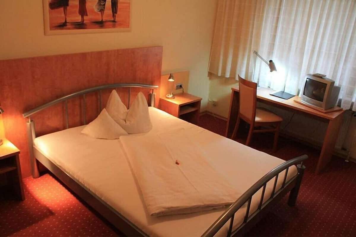 Habitación de hotel con cama, escritorio, silla, televisión y un cuadro en la pared.