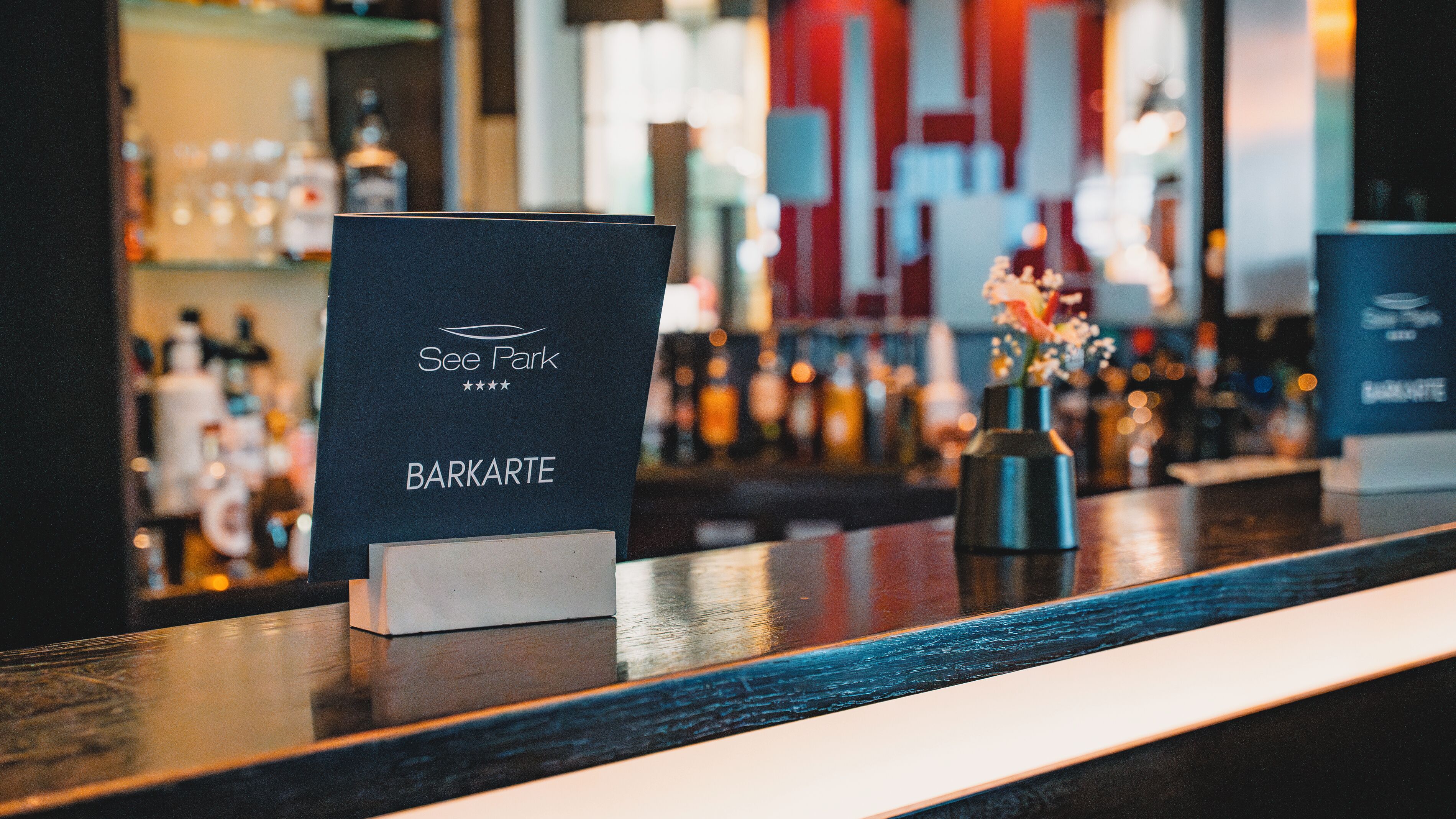 A bar counter with a sign for 'See Park BARKARTE' and a decorative vase with flowers.