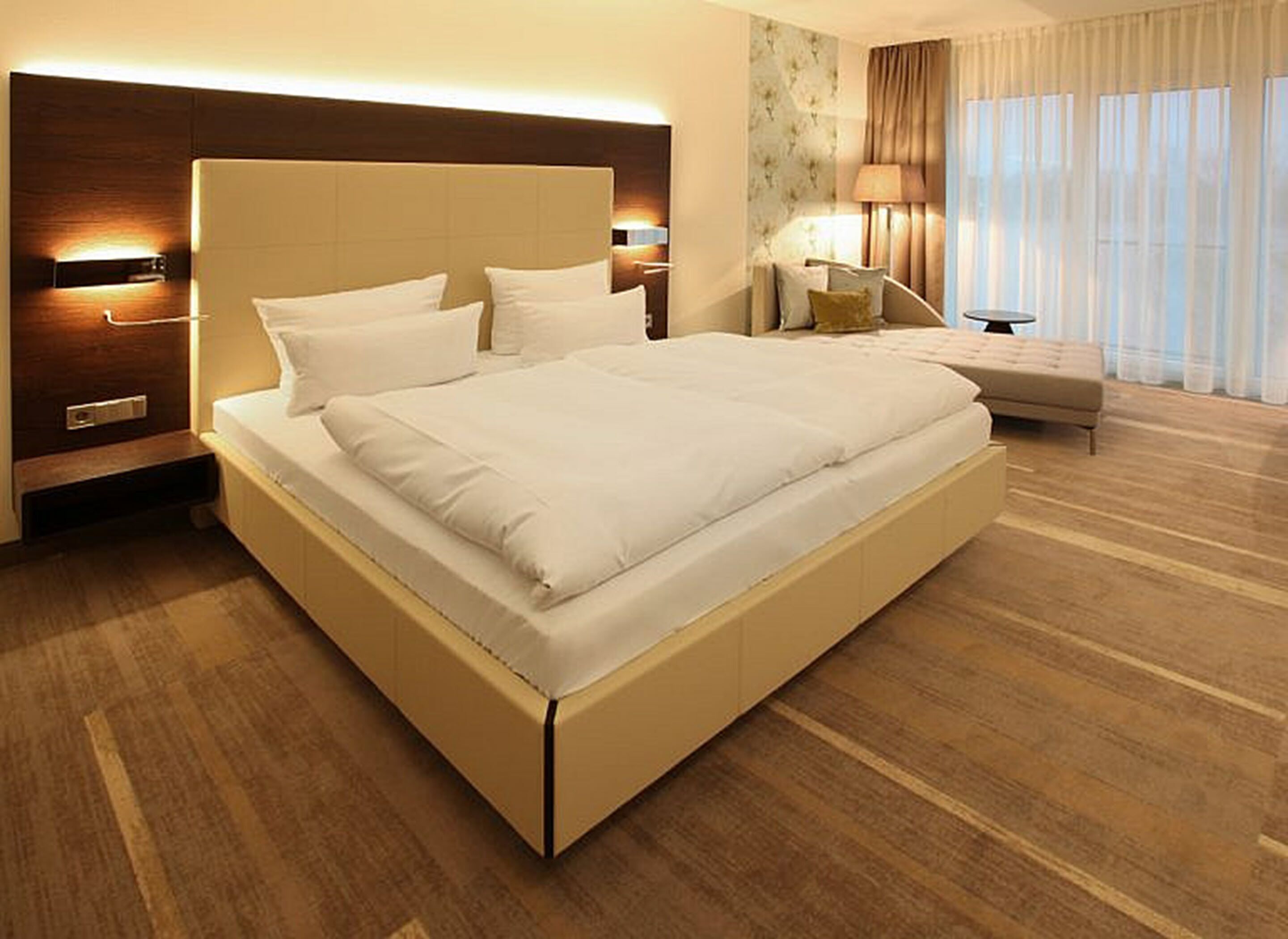 A modern hotel room with a large bed, a bedside table, a lamp, and a chair.