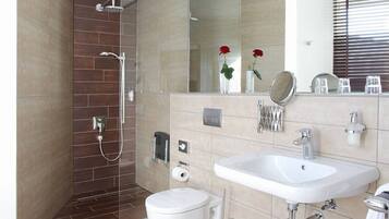Un baño moderno con ducha, inodoro, lavamanos y un espejo grande.