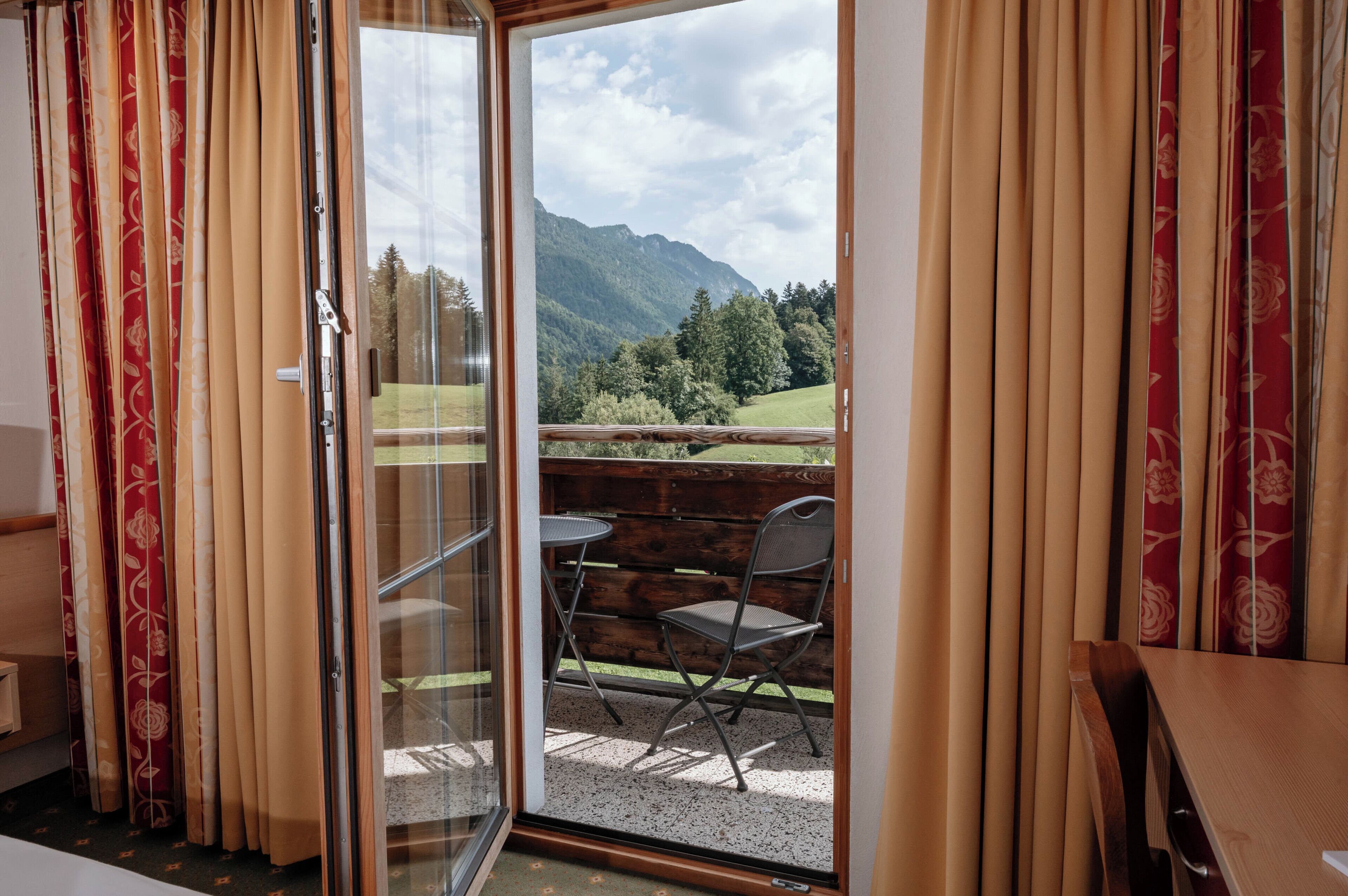 Una habitación con puerta de cristal corredera que da a una zona de estar exterior con vistas a las montañas.