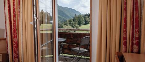 A room with a sliding glass door leading to an outdoor seating area with a view of mountains.