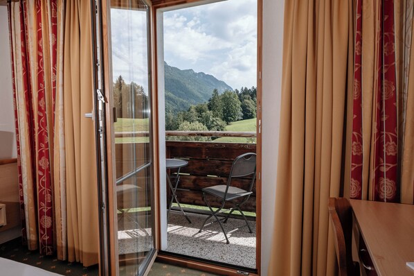 A room with a sliding glass door leading to an outdoor seating area with a view of mountains. - Hotel Mariasteiner Hof (Mariastein)