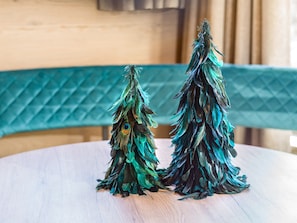 Dos árboles navideños decorativos hechos de plumas sobre una mesa redonda de madera.