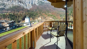 A wooden balcony with two patterned chairs, overlooking a mountainous landscape with a small tower and buildings in the valley. - Hotel Mariasteiner Hof (Mariastein)