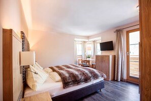 A bedroom with a bed, a desk, a chair, a TV, and a sliding door to a balcony. - Hotel Mariasteiner Hof (Mariastein)