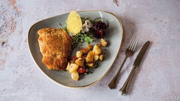 A plate with a breaded cutlet, roasted potatoes, and a small salad with a berry sauce.