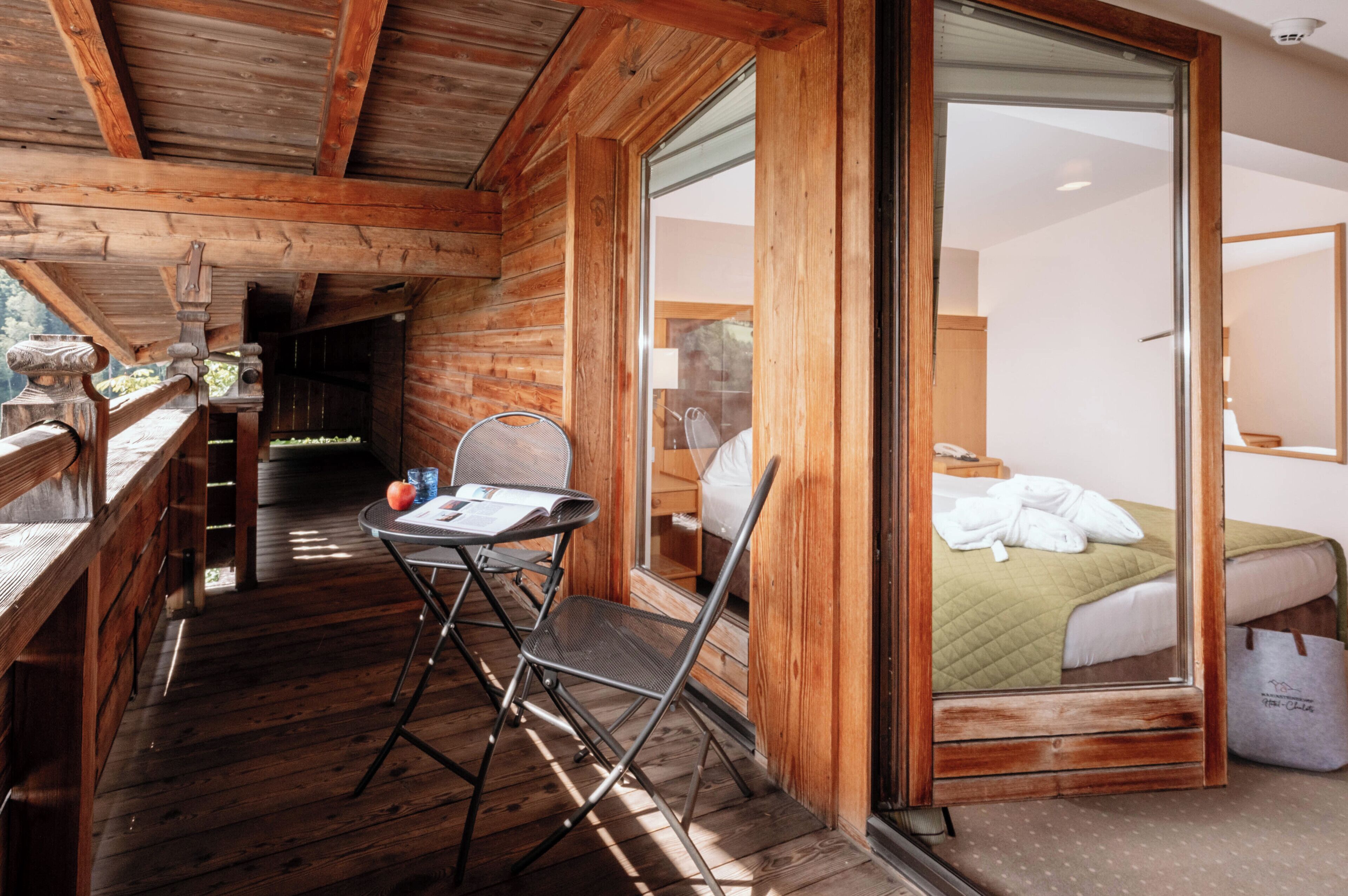 A wooden cabin with a balcony, a foldable table, and a bed with a green blanket.