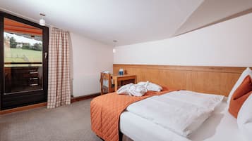 Une chambre d’hôtel avec un lit, une tête de lit en bois, une fenêtre donnant sur un espace verdoyant et un radiateur.