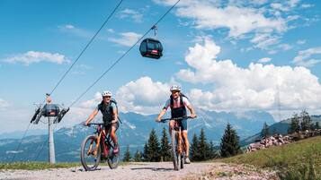 Dos ciclistas en una carretera de montaña, con un teleférico al fondo.