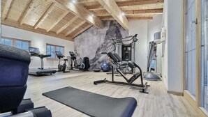 A gym with treadmills, elliptical machines, a squat rack, and a wall with a stone-like texture. - Hotel Mariasteiner Hof (Mariastein)