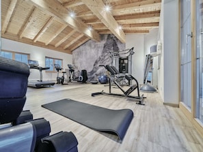 Un gimnasio con cintas de correr, elípticas, una jaula para sentadillas y una pared con textura similar a la piedra.