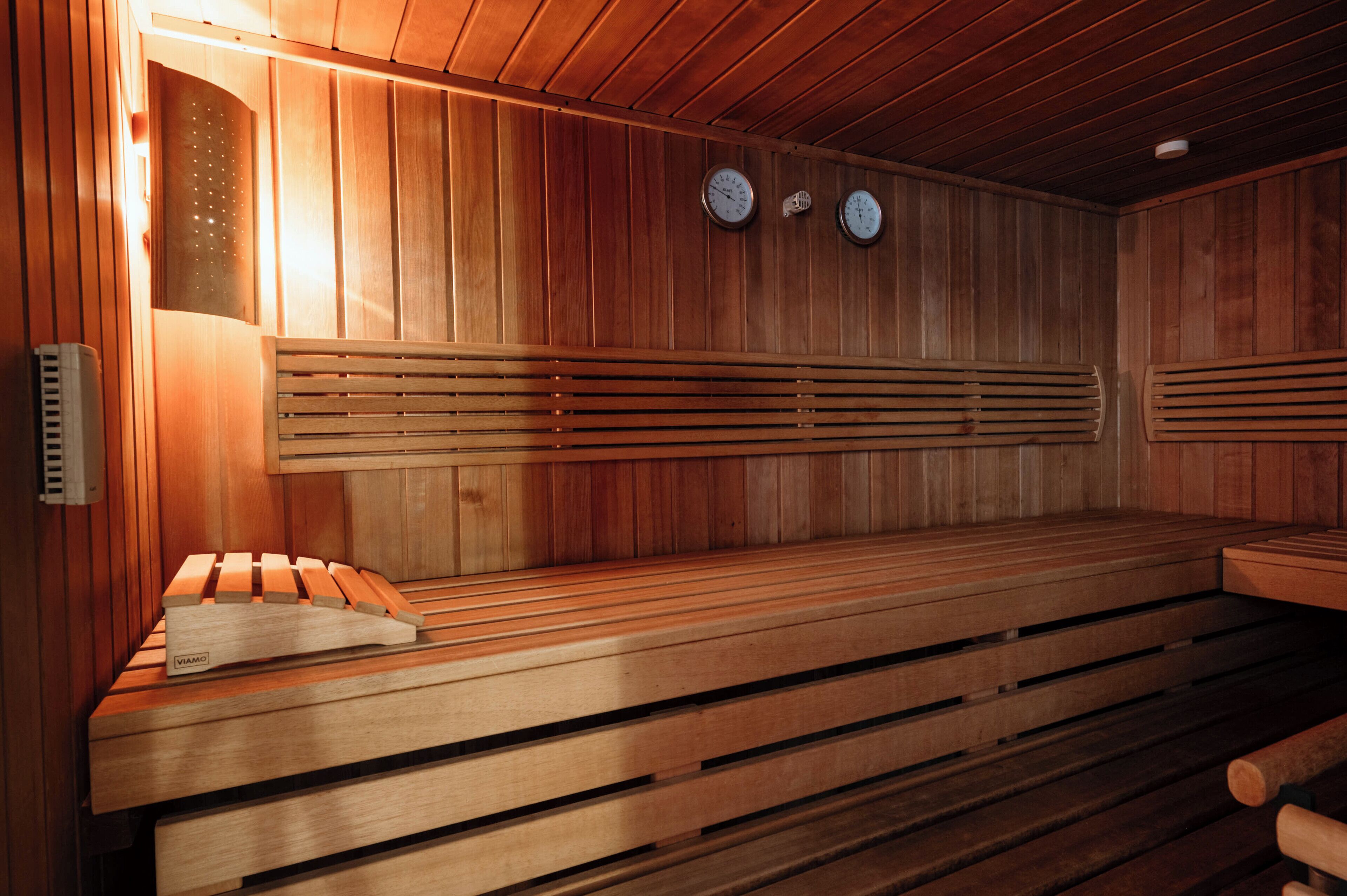 A sauna with wooden benches, a wall-mounted heater, and two wall clocks.