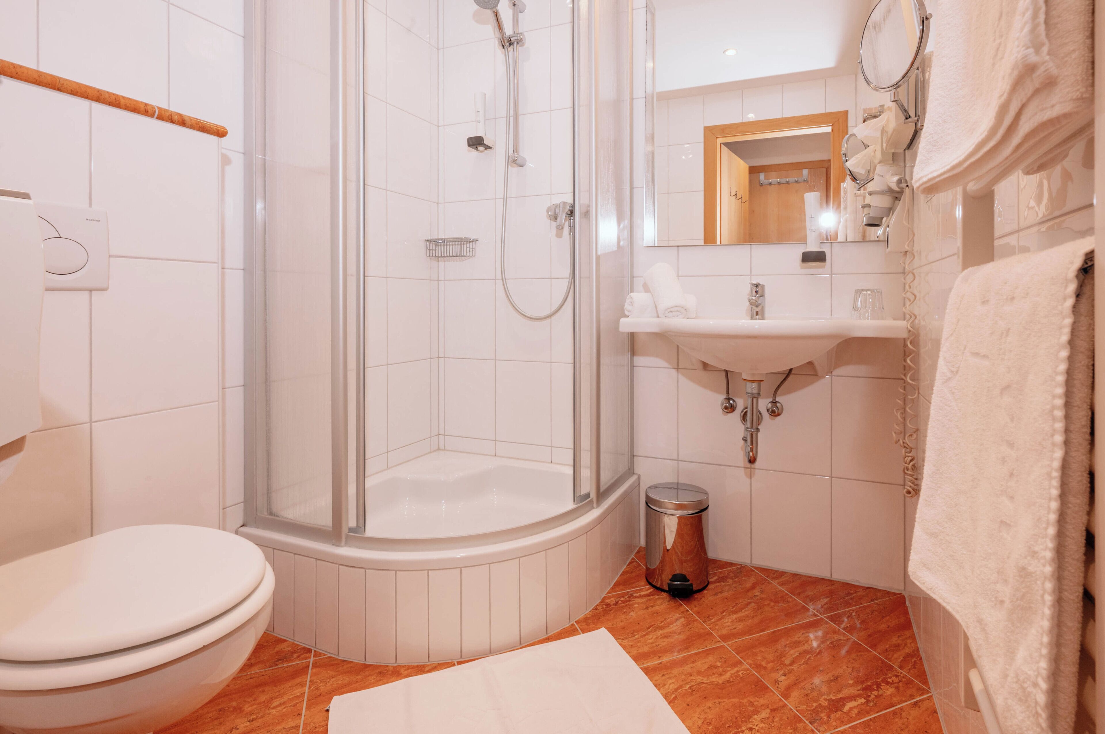 A modern bathroom with a glass-enclosed shower, a toilet, a sink, and a trash bin.