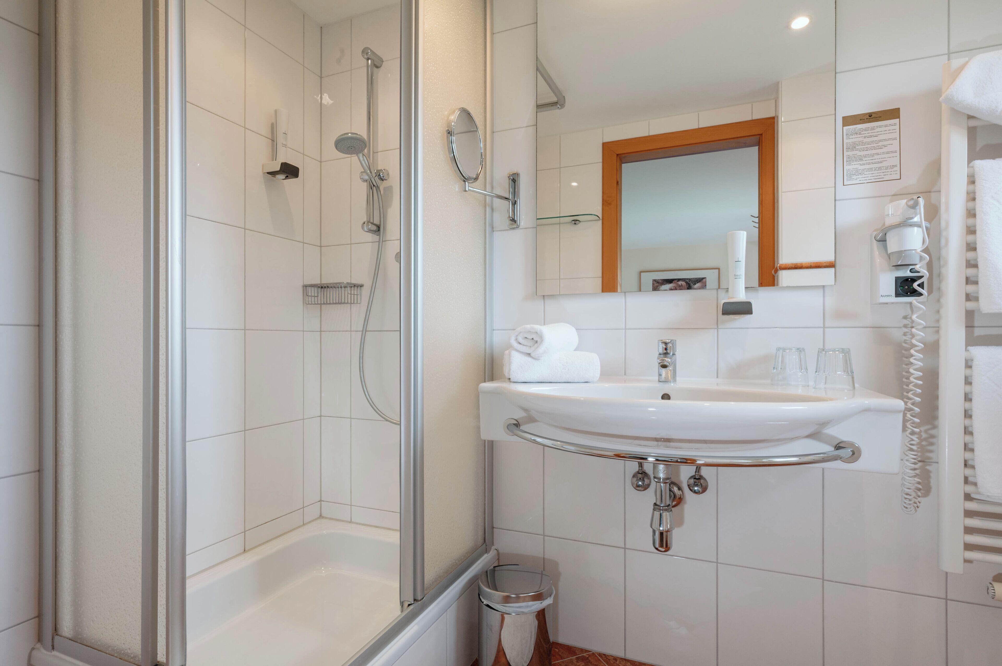 A modern bathroom with a glass-enclosed shower, a white sink with a chrome faucet, and a mirror above the sink.