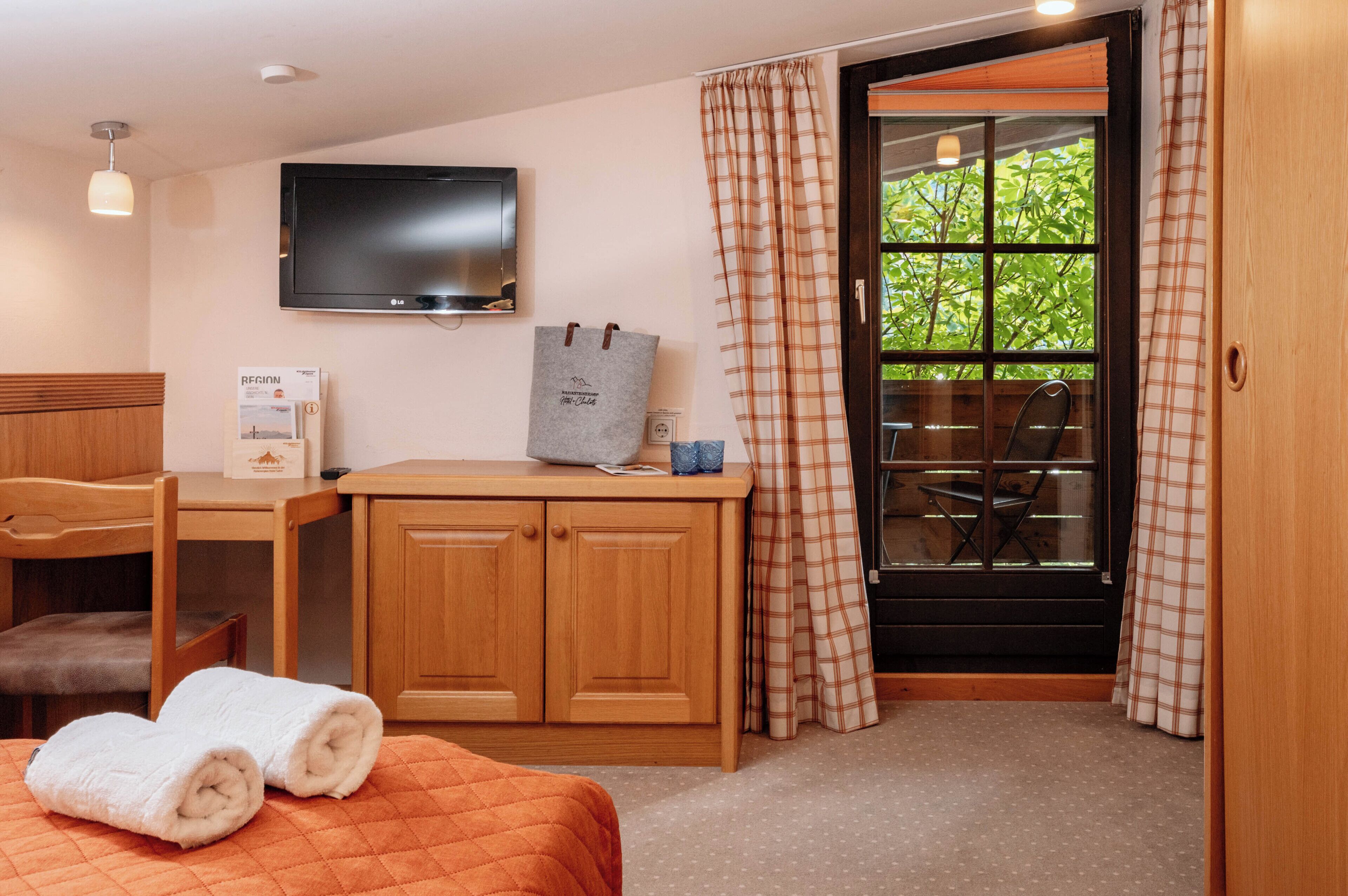 A hotel room with a bed, a desk, a television, and a window with curtains.