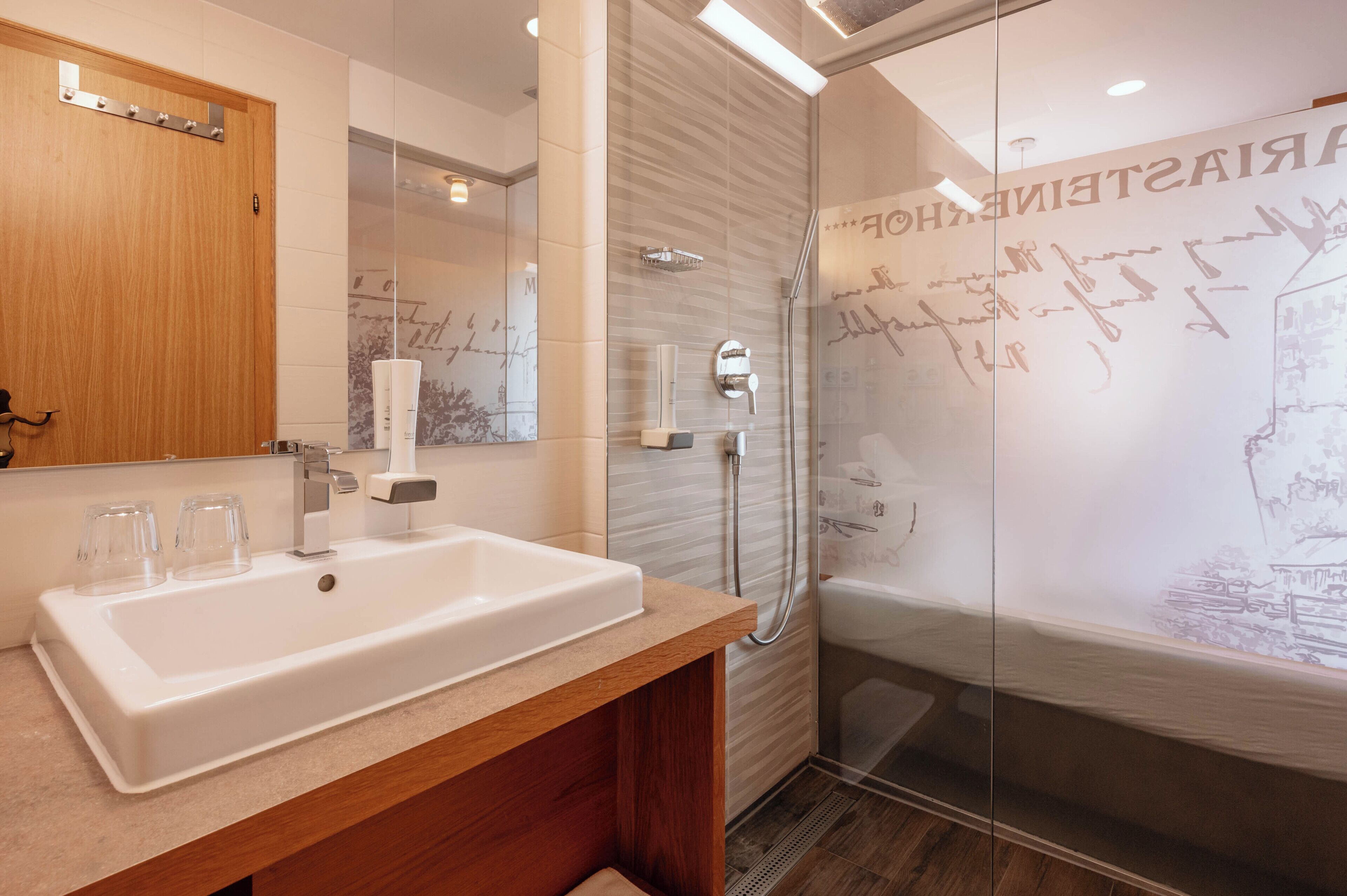 A modern bathroom with a large white sink, a mirror, and a glass-enclosed shower area.