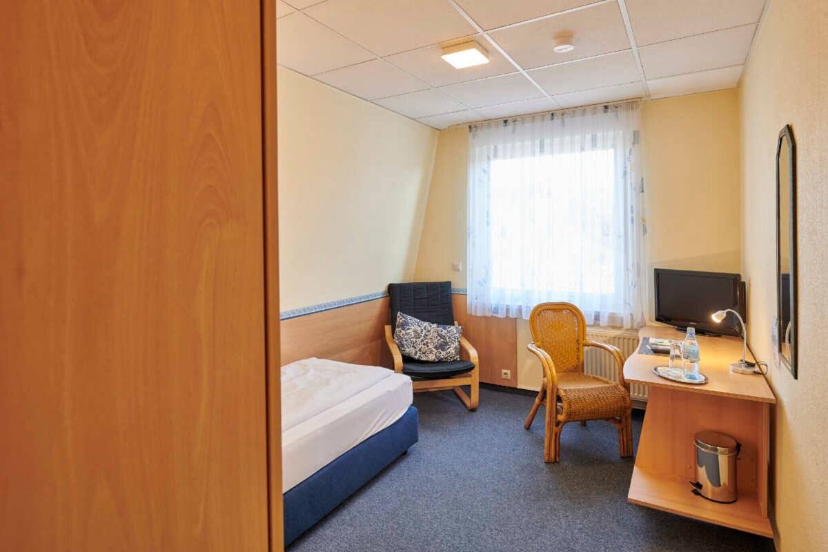 Een hotelkamer met een eenpersoonsbed, twee stoelen, een bureau met een computer, een televisie en een radiator.